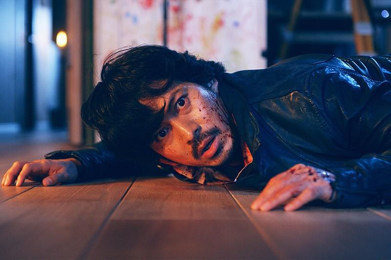 映画『来る』の場面写真。顔に血のついた野崎(岡田准一)が床に伏せている